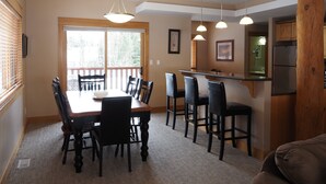 A dining area with a wooden table and chairs, a kitchen area with a refrigerator, and a window with blinds. - 4 BD/3BA Redstone Chalets E (Rossland)