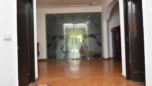 A hallway with wooden flooring, a patterned rug, and a glass door with a reflection. - Remarkable 6-bedroom Farmhouse in South Delhi (New Delhi)