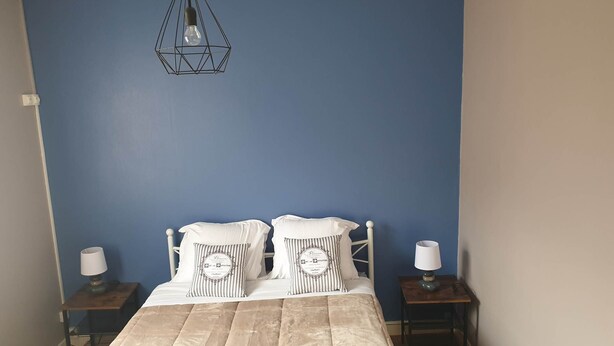 Een slaapkamer met een bed, twee nachtkastjes, een hanglamp en een blauwe wand.