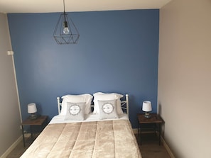 A bedroom with a bed, two bedside tables, a hanging light fixture, and a blue wall.