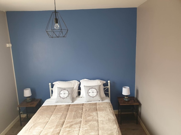 Ein Schlafzimmer mit einem Bett, zwei Nachttischen, einer Hängeleuchte und einer blauen Wand.
