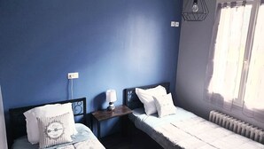 Een kamer met twee bedden, een nachtkastje met een lamp, een hanglamp en een raam met gordijnen.