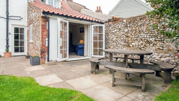 A stone house with a patio, a wooden table, and a blue chair. - Cosy Norfolk Cottage (King's Lynn)
