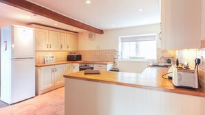 A modern kitchen with white cabinets, a wooden countertop, a built-in oven, and a window providing natural light. - Cosy Norfolk Cottage (King's Lynn)