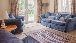 A living room with a blue sofa set, a patterned rug, and a lamp on a wooden side table. - Cosy Norfolk Cottage (King's Lynn)