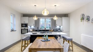 A modern kitchen with white cabinets, a central island, pendant lighting, and a dining area with white chairs.