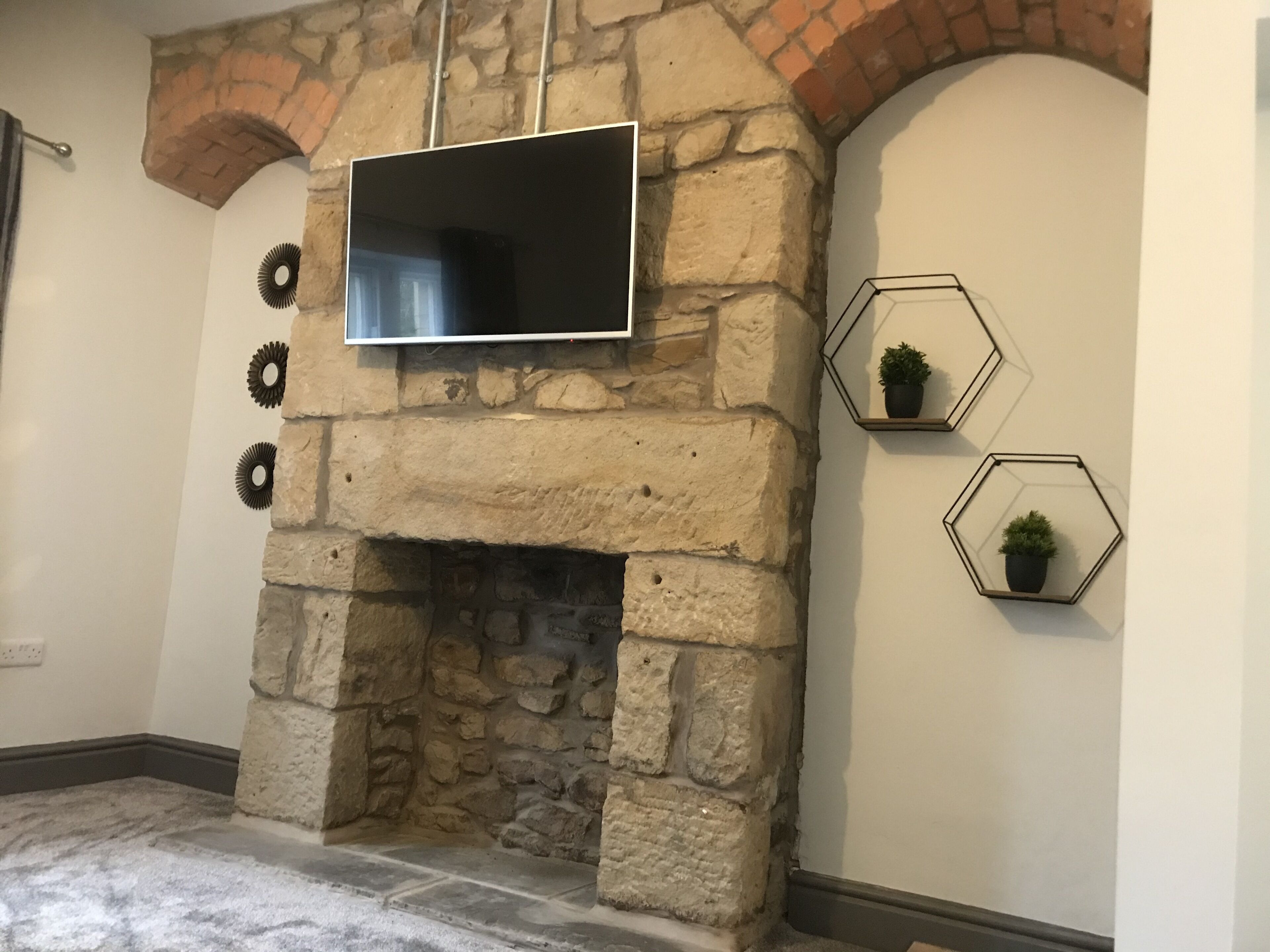A stone fireplace with a flat-screen TV mounted above it, surrounded by hexagonal wall decorations.