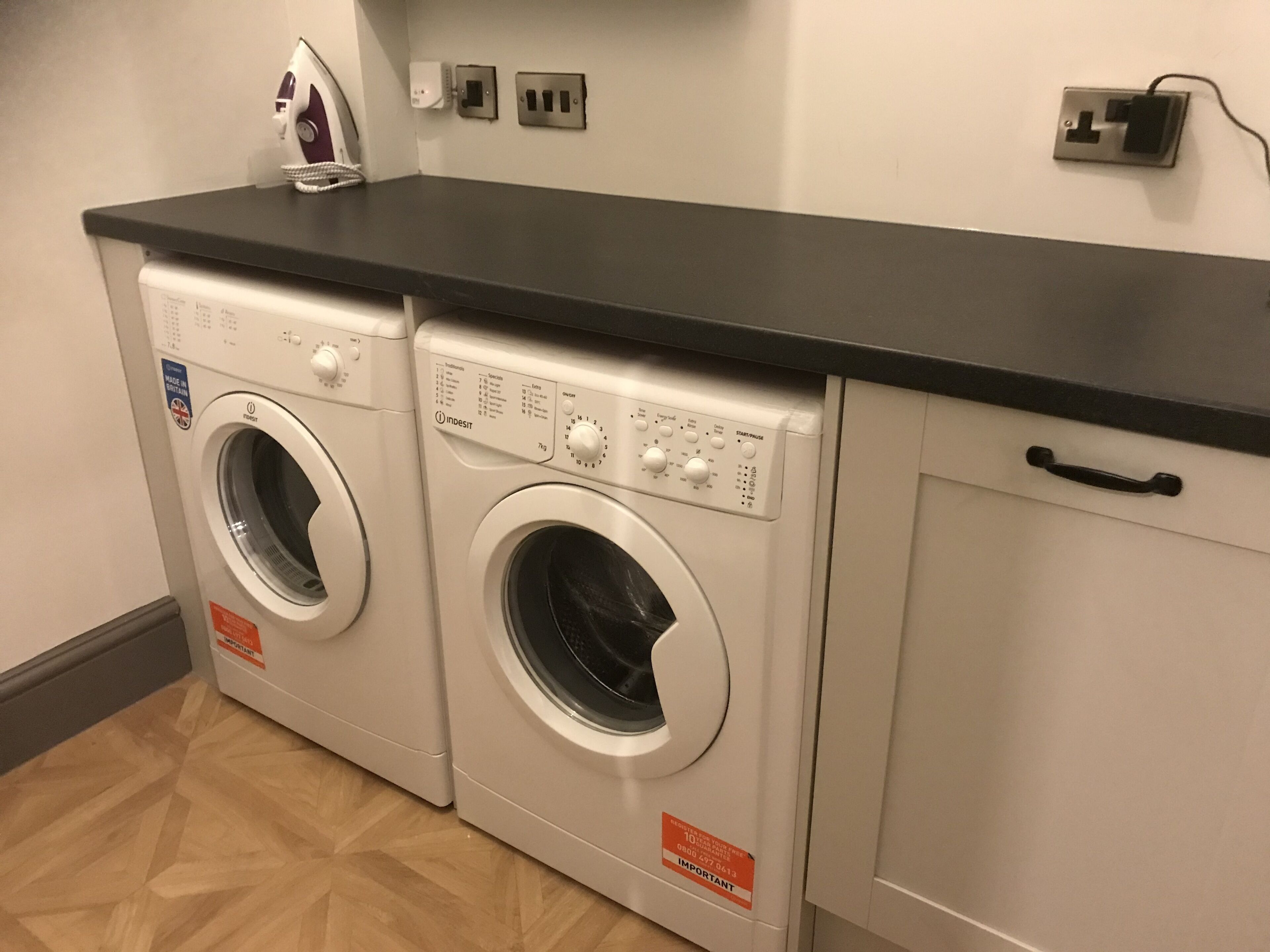 A laundry area with two front-loading washing machines, a black countertop, and a white cabinet with a handle.