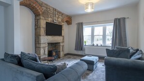 A living room with a stone fireplace, grey sofas, and a large window with curtains.