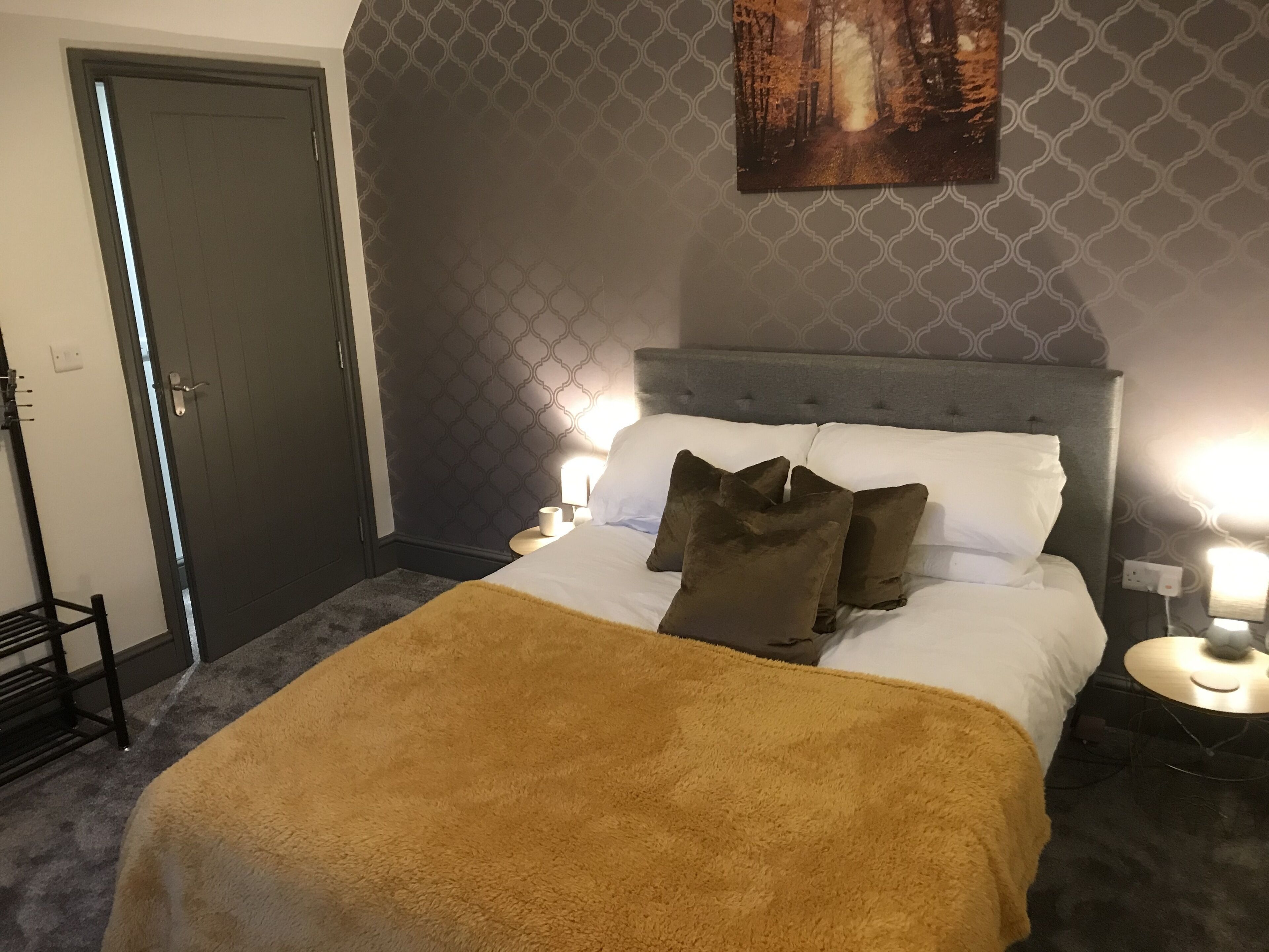 A bedroom with a bed, two bedside tables with lamps, a door, and a patterned wall.