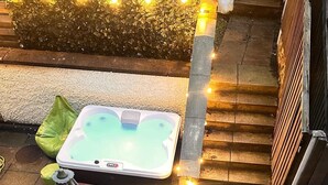 A hot tub with a small table and chairs, surrounded by a stone pathway and a wooden fence.