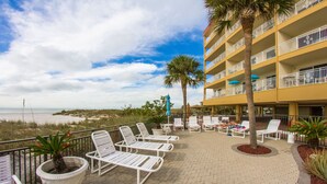 A hotel balcony with white lounge chairs, a palm tree, and a view of the beach.