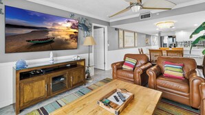 A living room with a large flat-screen TV, leather sofas, a wooden coffee table, and a ceiling fan. - Luxury Beach Front Corner Beach Place #306 (Madeira Beach)