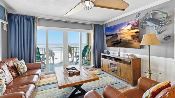 A living room with a leather sofa, a wooden coffee table, and a television on the wall. There is a balcony with a view of the ocean. - Luxury Beach Front Corner Beach Place #306 (Madeira Beach)