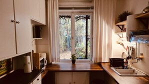 Une cuisine de taille réduite, dotée d’une fenêtre, de meubles blancs, d’un évier et d’une cuisinière.