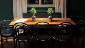 Un coin repas avec une table en bois, quatre chaises, deux plantes en pot et une fenêtre avec des rideaux.