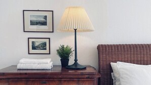 Un lit bien fait, avec du linge de lit blanc, une table de chevet en bois sur laquelle se trouve une lampe, et deux tableaux encadrés accrochés au mur.