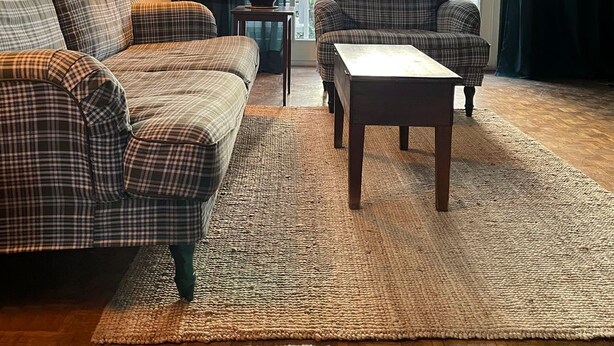 Un salon avec un mur vert foncé, une grande fenêtre, un canapé à carreaux, un fauteuil assorti, une petite table et un lampadaire.