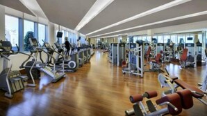 A modern gym with cardio machines, weight stations, and a wooden floor. - Fashion Avenue Dubai Mall Residences - Studio with balcony (Dubai)