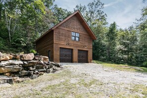 A wooden cabin with a gabled roof, two garage doors, and a stone wall in front.