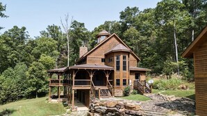 Een houten chalet met een veranda, stenen trappen en een stenen schoorsteen.