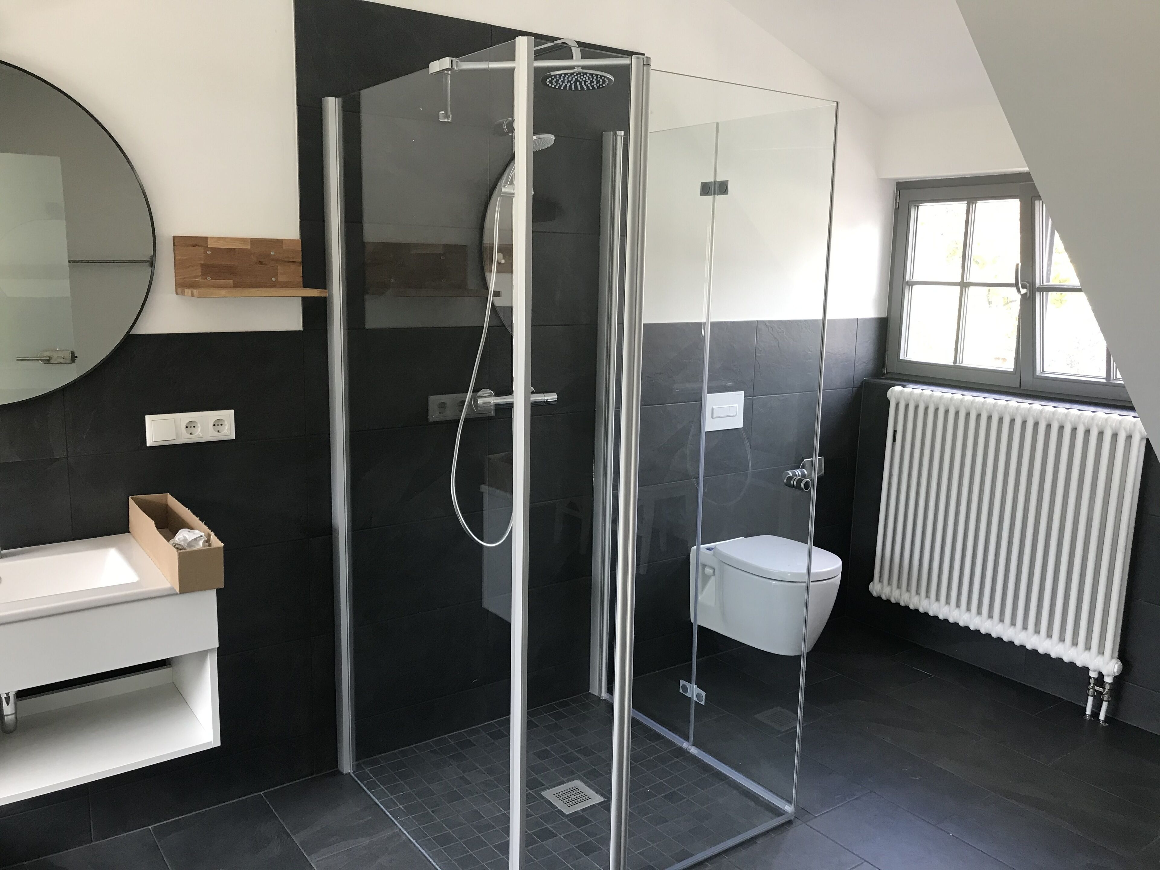 A modern bathroom with a glass-enclosed shower, a white toilet, a sink with a mirror, and a window providing natural light.