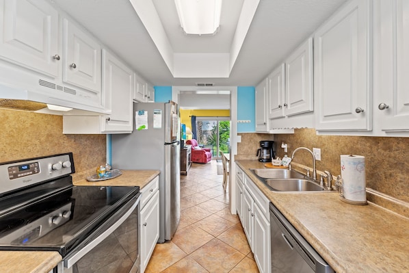 A modern kitchen with white cabinets, a stainless steel refrigerator, a built-in oven, and a granite countertop.