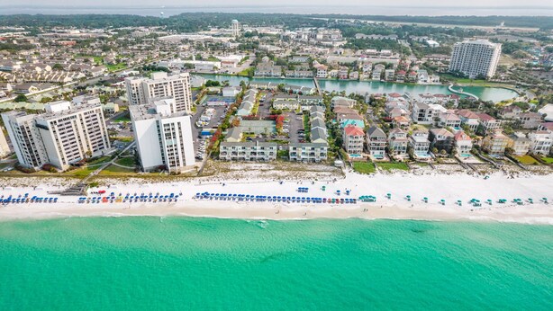 Vista aerea di un resort costiero con ville sulla spiaggia, un porto turistico e una spiaggia con ombrelloni.