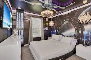 A bedroom with a large bed, a ceiling fan, a TV, and Star Wars-themed decor.