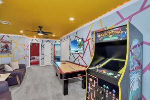 Una habitación con una máquina de pinball, una mesa de billar y un ventilador de techo.