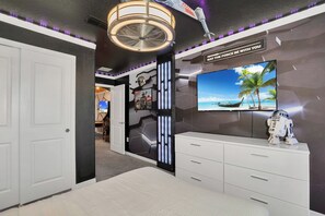 Ein Zimmer mit einem großen Flachbildfernseher an der Wand, einem Deckenventilator und einer Star Wars-Dekoration, darunter eine lebensgroße R2-D2-Figur.