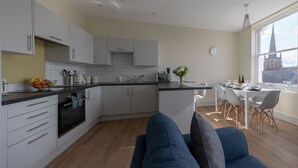 A modern kitchen with white cabinets, a built-in oven, and a dining area with a table and chairs. - Apartment 5 Isabella House Hereford (Hereford)