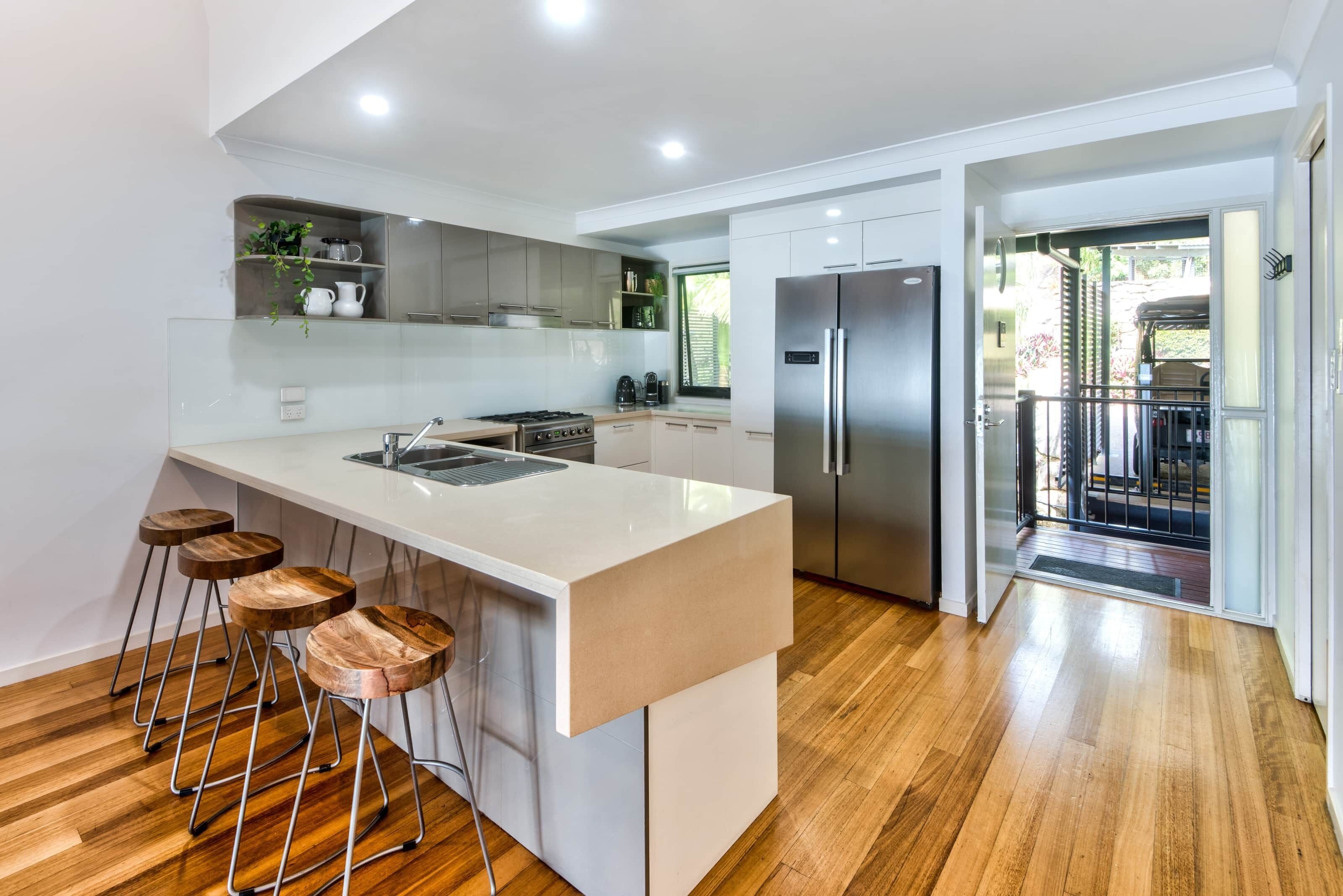 A modern kitchen with a central island, bar stools, and a stainless steel refrigerator.