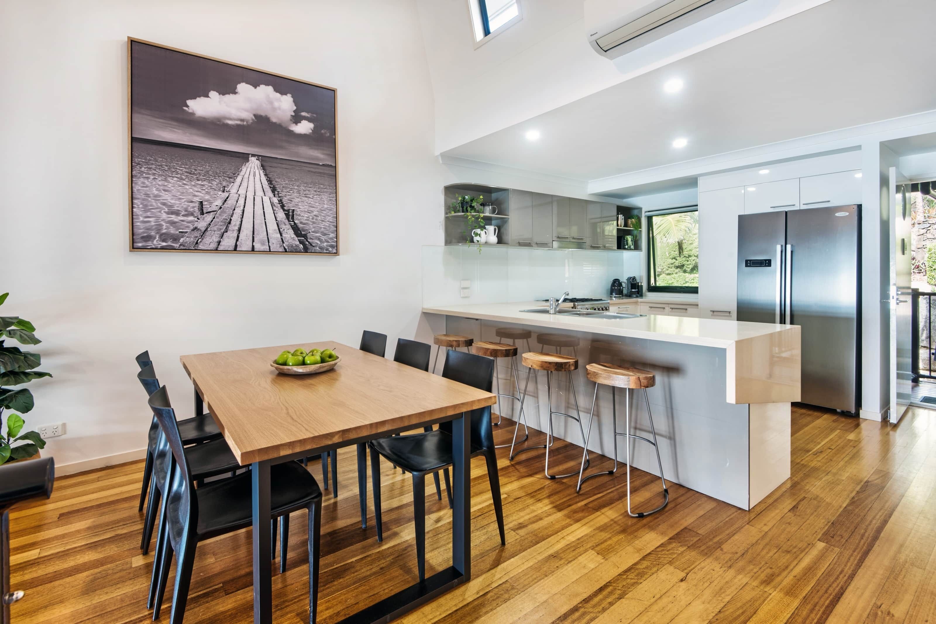 A modern kitchen with a central island, bar stools, and a dining area with a wooden table and chairs.