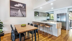 Une cuisine moderne dotée d’un îlot central, de tabourets de bar et d’un coin repas avec une table et des chaises en bois.