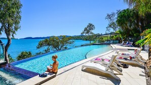Un espace aménagé au bord de la piscine, avec des chaises longues, un coin salon abrité et une vue sur la mer.