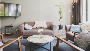 Una sala de estar moderna con un sofá, una mesa de centro con un jarrón de flores, una lámpara de pie y un televisor montado en la pared.
