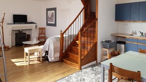 A cozy living room with a wooden staircase, a fireplace, a dining area, and a kitchen with blue cabinets. - House La Galinette 9 people Heated swimming pool Hammam Jacuzzi Sauna (Izeaux)