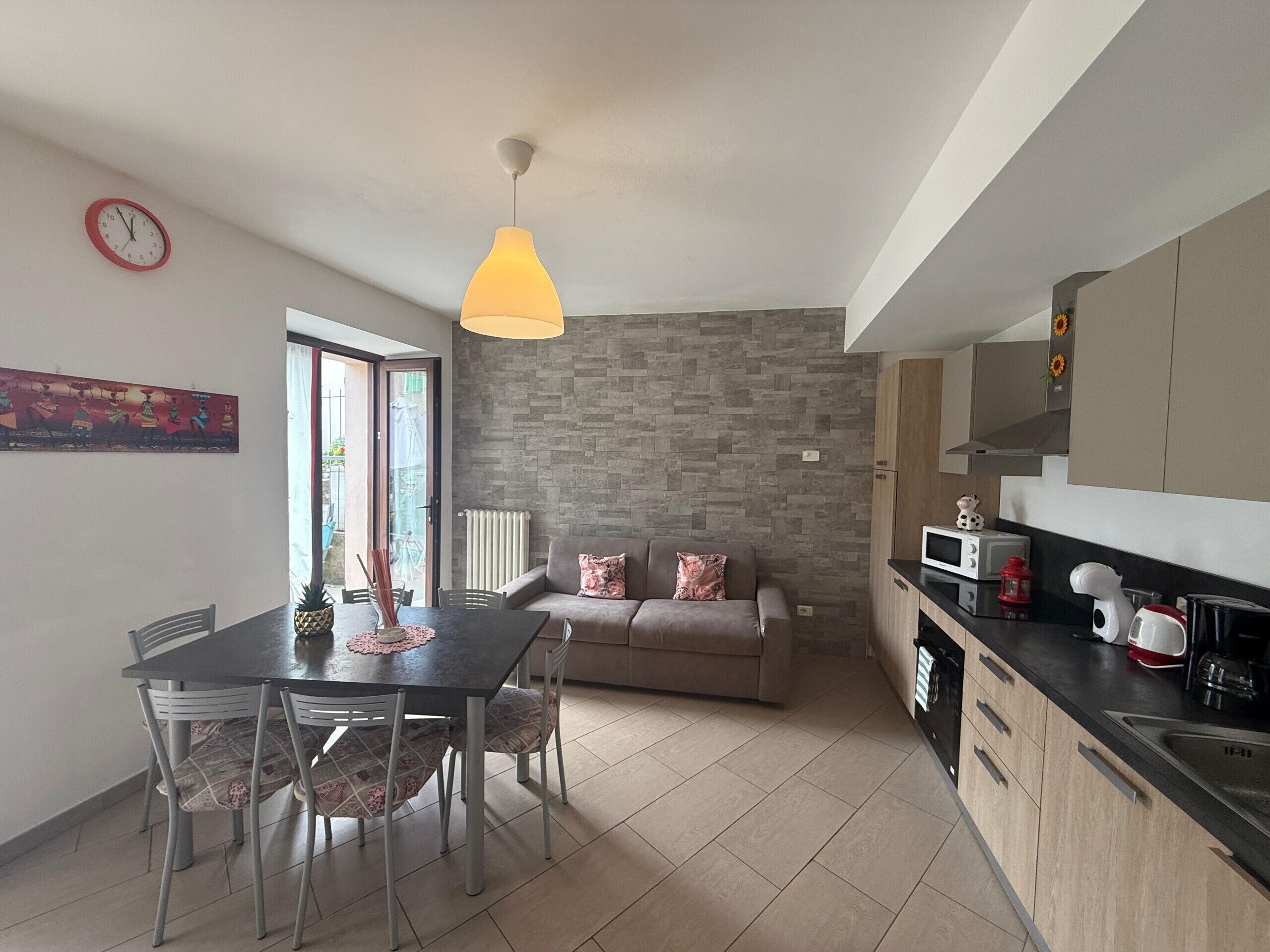 Une cuisine moderne avec un mur de crédence en pierre, un coin repas avec une table et des chaises, un canapé et un luminaire suspendu.