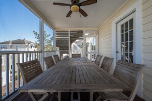 Een houten terras met een tafel, stoelen, een plafondventilator en uitzicht op omliggende huizen.