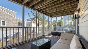 A covered deck with a glass-top table, beige sofa, and a wicker bench.