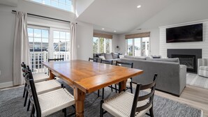 A spacious living room with a wooden dining table, grey sofa, and a fireplace.