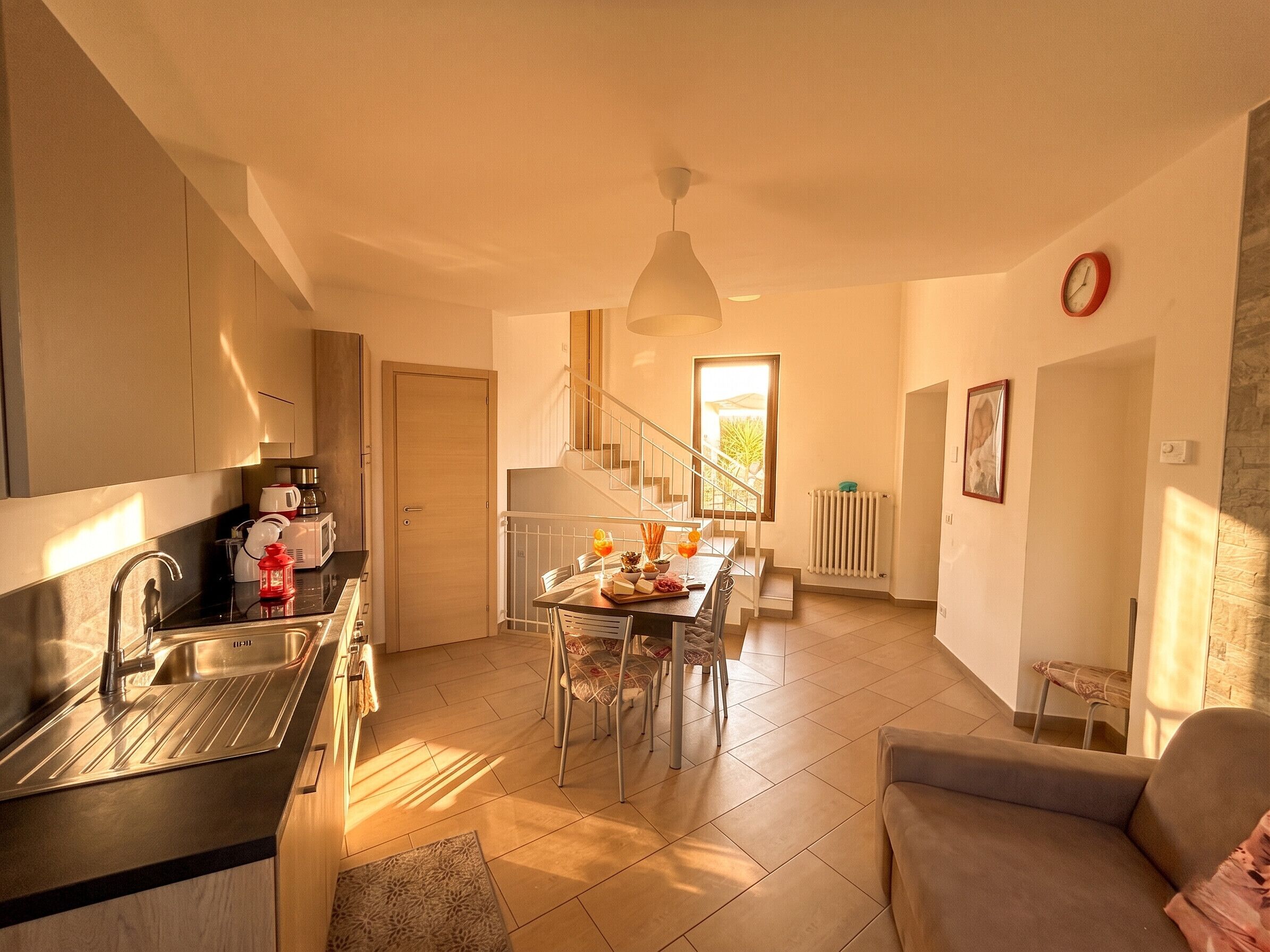 A modern kitchen with a dining area, a staircase, and a living room with a sofa.