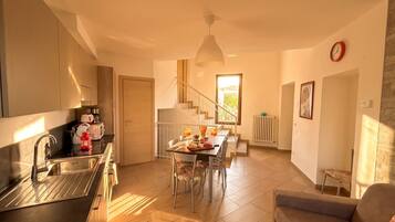 A modern kitchen with a dining area, a staircase, and a living room with a sofa.