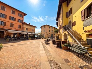 Une rue pavée avec des tables en terrasse, un restaurant appelé « Ristorante Miralago » et un bâtiment doté d’un escalier et d’une enseigne indiquant « Dispensazione Donatale ».