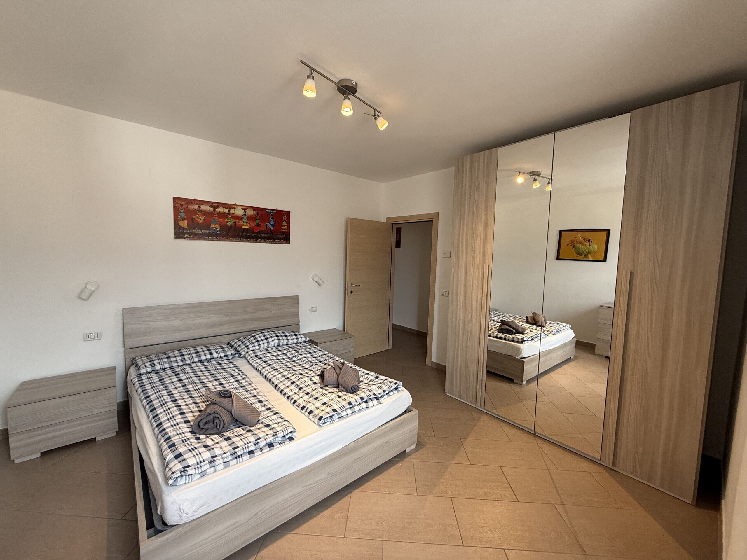 Un dormitorio con cama, armario, espejo y un cuadro en la pared.