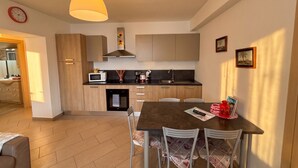 Una cocina moderna con armarios de madera, un microondas y un lavamanos. Hay una mesa de comedor con sillas y una lámpara colgante encima.