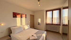 Un dormitorio con cama, mesita de noche, decoración en la pared, ventana con cortinas y un radiador.