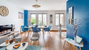 A modern living room with a dining area, large windows, and a blue accent wall.