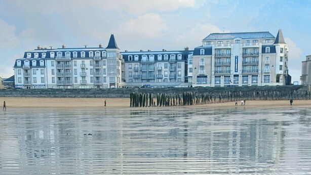 A beachfront hotel with multiple balconies and a sandy beach in the foreground.